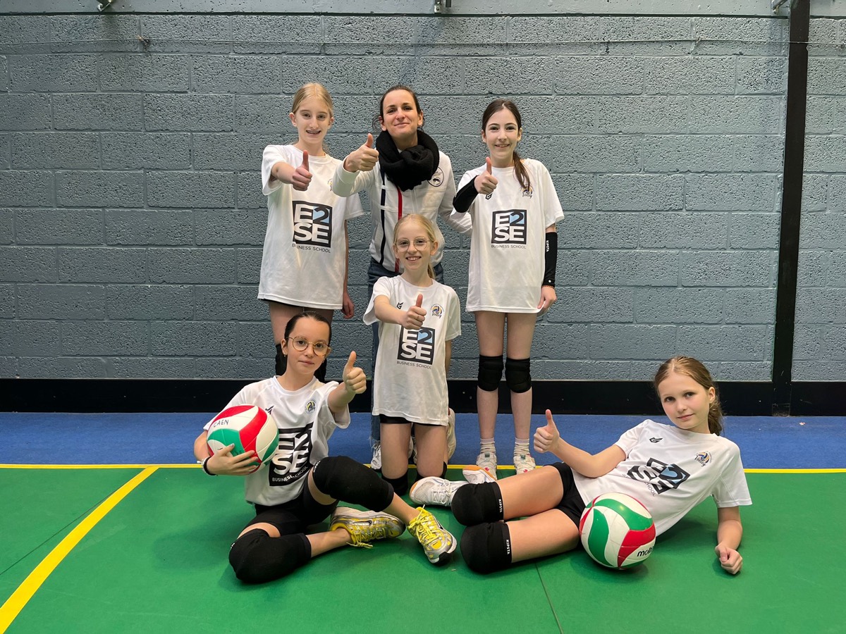 Jeunes joueuses et une adulte, pouces levés, deux ballons de volley au premier plan