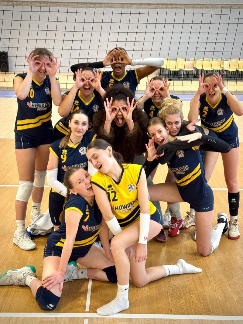 Équipe de joueuses en maillots bleu nuit et jaune, les mains devant les yeux en forme de lunettes
