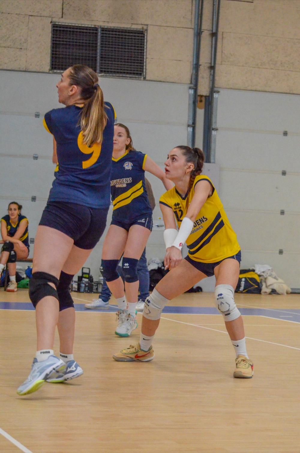 Deux joueuses en maillots bleu nuit et jaune se placent pour recevoir le service