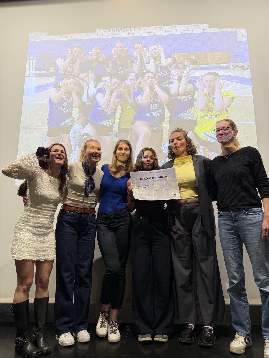 Groupe de personnes posant avec un diplôme d’honneur devant la photo d’équipe projetée